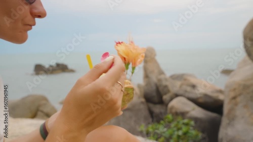 Woman Eating Colorful Ice Cream from a Coconut Shell Decorated with Flowers while Sitting Near Iconic Hin Ta Hin Yai Rocks on Samui Island, Tropical Dessert Concept