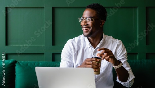 Happy african american man working on laptop with coffee in modern green office
