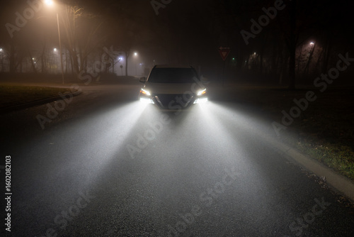 Headlights from a white SUV illuminate mist on a foggy night