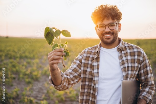 Bild auf Leinwand Agronomist Holding Soybean Plant in Cultivated Field at Sunset