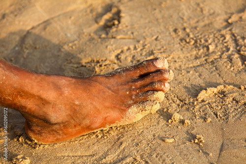 Fototapeta Naklejka Na Ścianę i Meble -  A foot is in the sand with a few footprints behind it