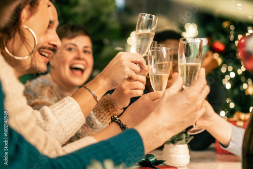 Group of diverse friends toasting with champagne and laughing at a party. Multi-ethnic people celebrating the holidays or New Year's Eve with a festive dinner together.