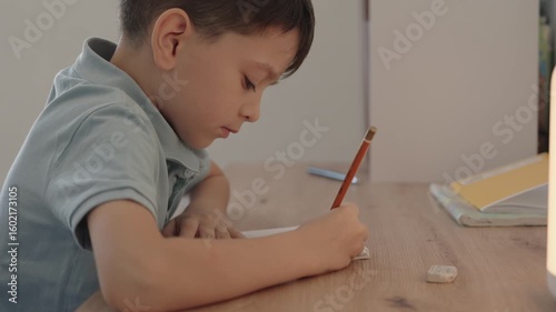 A young boy sits at his desk and writes in a notebook. He is focused and diligently completing his schoolwork.
