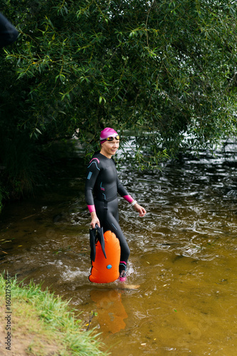 Woman in a wetsuit and a buoy enters the water on lake