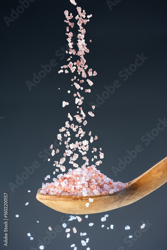 Heap of rose-colored sea salt fall from above onto a wooden spoon, great for kitchen and mineral nutrition images.
