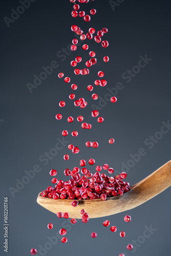 Aromatic dried spice berries fall from above onto a wooden spoon, ideal for gourmet cooking and natural themes.