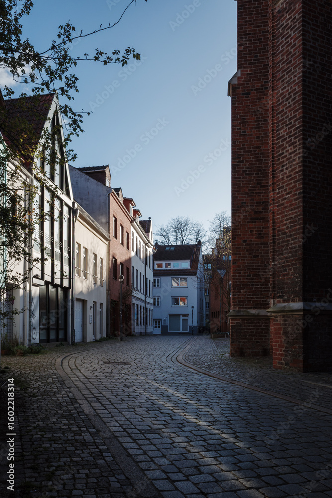 Obraz premium A narrow cobblestone street curves through a historic district of Bremen, Germany, flanked by traditional European buildings with varied facades.