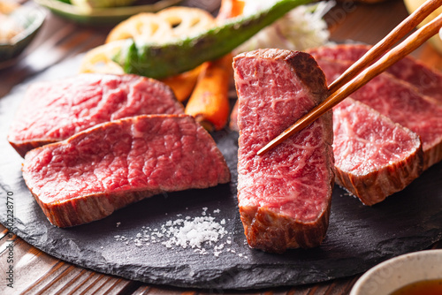【黒毛和牛ステーキ】レアで美しく焼き上げた黒毛和牛モモ肉のステーキ。ジューシーな肉の旨みを引き立てるのは、素揚げした季節の野菜と彩り豊かな薬味。わさびや塩、日本酒とともに、和の美味を贅沢に味わう一皿です。