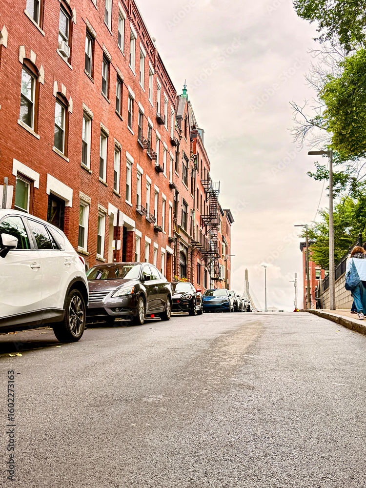 Obraz premium Steep residential street lined with red brick buildings and parked cars