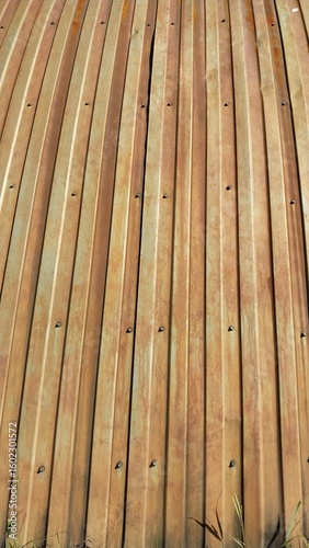  A close-up view of light brown wooden planks arranged in parallel lines, forming a smooth and uniform surface with visible grain patterns and small screw fasteners