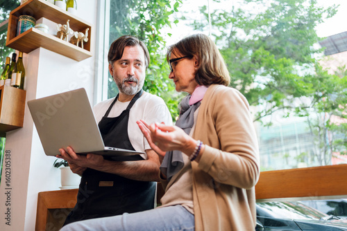 Cafe owner and business advisor discussing marketing or finance using smart phones. Both are smiling and engaged, symbolizing teamwork, strategy, and modern small business collaboration.