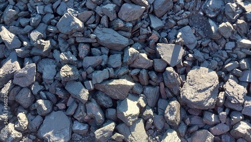 A close-up view of a pile of gray gravel and small rocks, showcasing natural textures and irregular shapes under bright sunlight