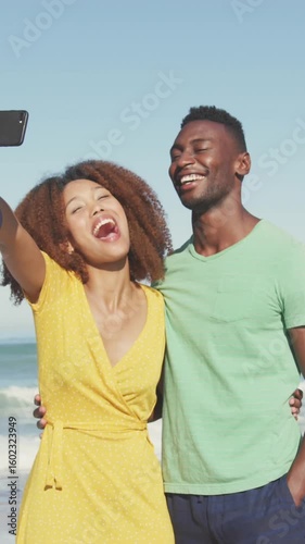 Animation of social media heart icons over smiling couple taking selfie with smartphone on beach