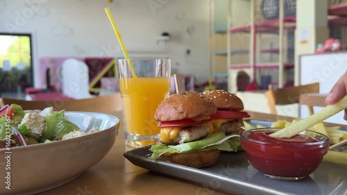 child eat mini cheeseburgers with lettuce and tomato is served alongside fries, salad, ketchup, and a glass of orange juice