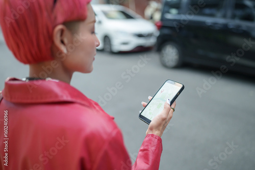 Traveler Gen z girl leather fashion with punk Asian woman tourist in city street searching location in map application online smart phone using GPS navigating