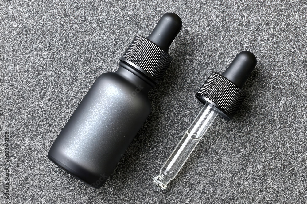 Naklejka premium Two dark gray, matte-finish dropper bottles on a gray textured surface