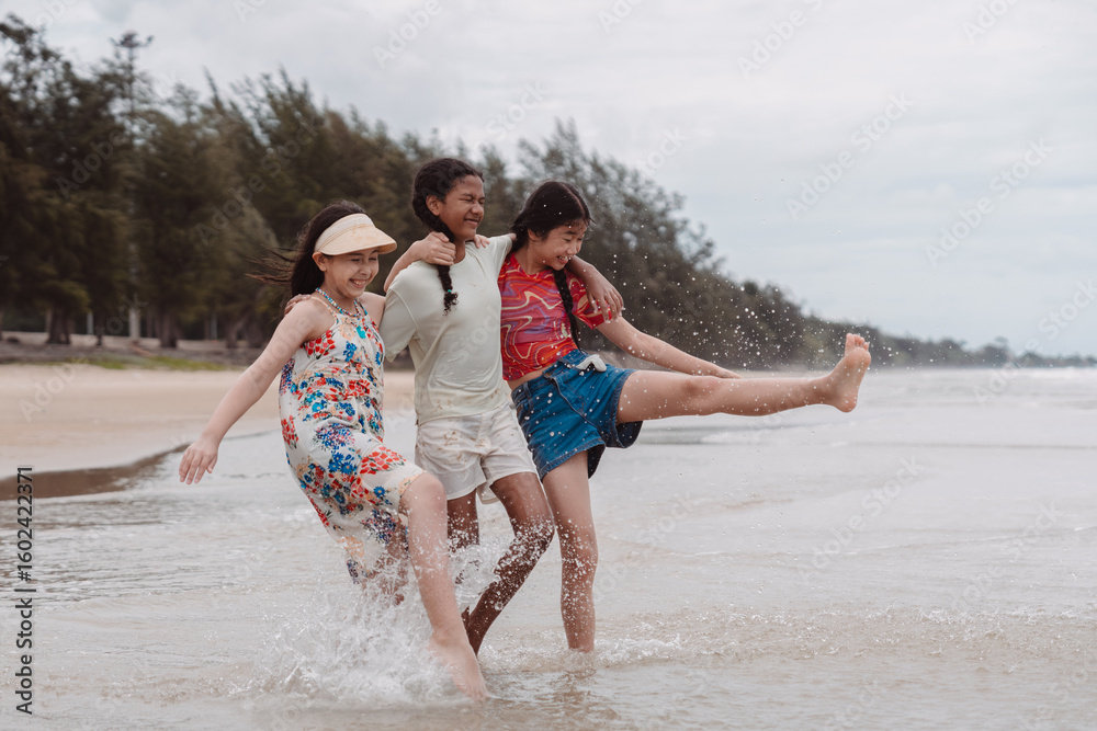 Obraz premium Asian and multicultural friends walking and splashing in beach water, enjoying childhood freedom, friendship, and outdoor fun in a playful and joyful summer moment.
