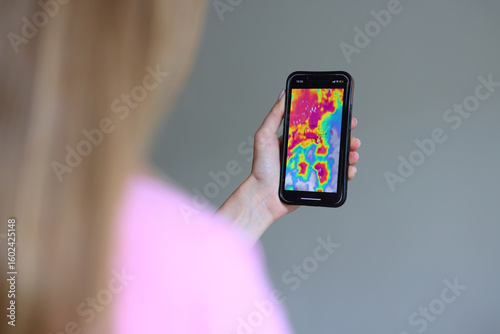 Woman checking mobile weather forecast during storm, high alert, real-time radar, safety planning.