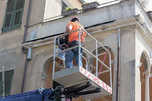 Operaio edile su piattaforma aerea che restaura la facciata di un edificio storico