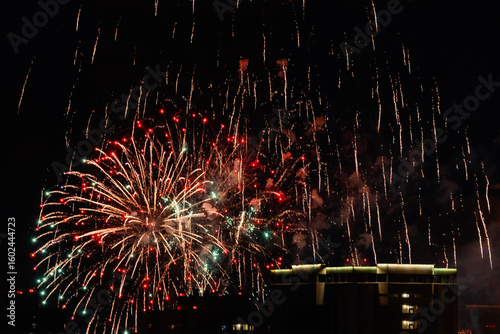 Vibrant fireworks explode in the night sky over a city building, creating a dazzling display of light and color