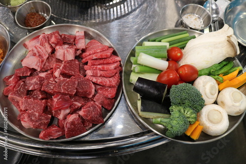 Korean Barbecue Grill Setup with Fresh Beef, Side Dishes, and Vegetables at Traditional Restaurant Table
