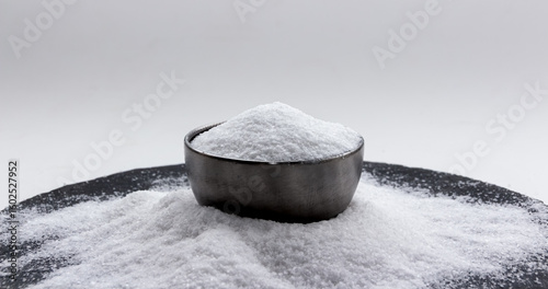 Iodized salt is in a metal container bowl, laying on a small pile of salt. Version I.
