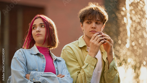 Φωτογραφία Young girl disappointed while boy eats suspicious burger near fountain