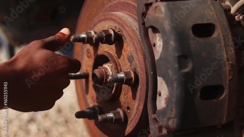 Close up of a man's hand screwing a lug not on a wheel hub of a car under maintenance