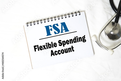 FSA - Flexible Spending Account on notebook. Bright white background and doctor's stethoscope. Medical and health concept.