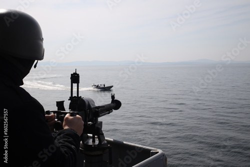 A military soldier defends a warship from an attacking boat.
