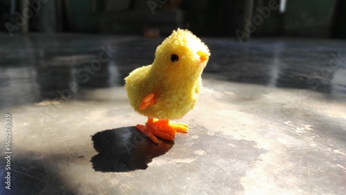 Close Up of a Yellow Toy Chicken with Orange Legs and Beak on Gray Surface