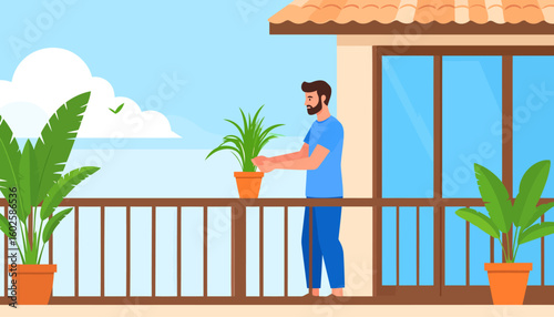 A bearded man in a blue t-shirt carefully tends to a green potted plant on a sunny balcony.