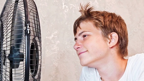 Photography Teenager boy suffering from the heat at home, he is sitting on the couch next to an electric fan