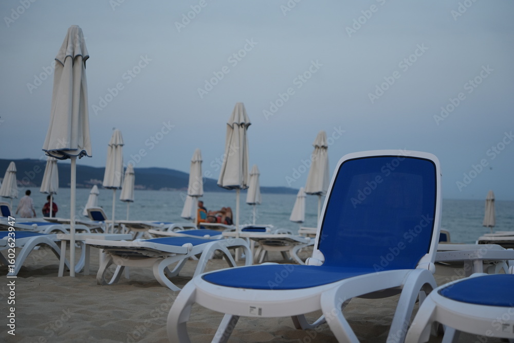 Obraz premium closed beach umbrellas and empty sun loungers on the coast of Golden Sands resort in Bulgaria, early morning or off-season, overcast sky and calm sea, tranquil beach scene