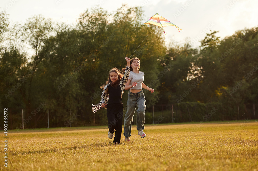 Fototapeta premium Two girls kids are playing with kite on the field