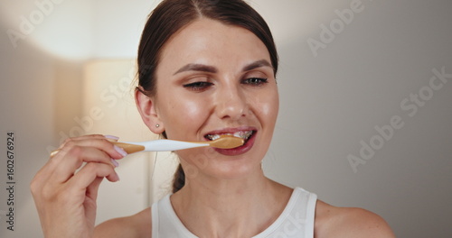 Young Caucasian woman with braces brushing teeth with toothbrush. Focus on dental care, hygiene, and healthy lifestyle. Image highlights importance of maintaining oral health habits with braces.