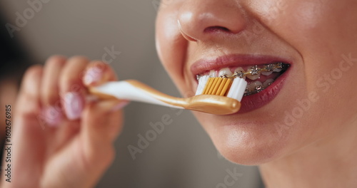 Young woman with braces practicing dental care, brushing teeth with toothbrush. Focus on oral hygiene and healthy smile.