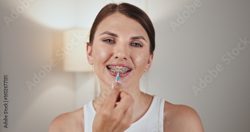 White female teenager with braces demonstrating dental care by using an oral irrigator. She smiles while holding irrigator near her braces, highlighting effective orthodontic hygiene practices.