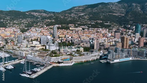Glamorous drone panorama of Monaco’s Larvotto coast: luxury super‑yachts, Casino de Monte‑Carlo domes, high‑rise skyline and sheer Maritime Alps plunging into the sapphire Mediterranean Sea.