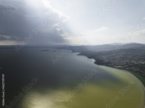 Aerial view of the tranquil Trasimeno Lake reflecting the sky, with the shoreline curving gently towards the distant hills, Torricella, Umbria, Italy.