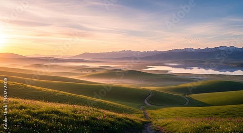 Scenic Landscape View of Rolling Green Hills, Mountains, and Calm Lake Under a Pastel Sky at Sunrise.