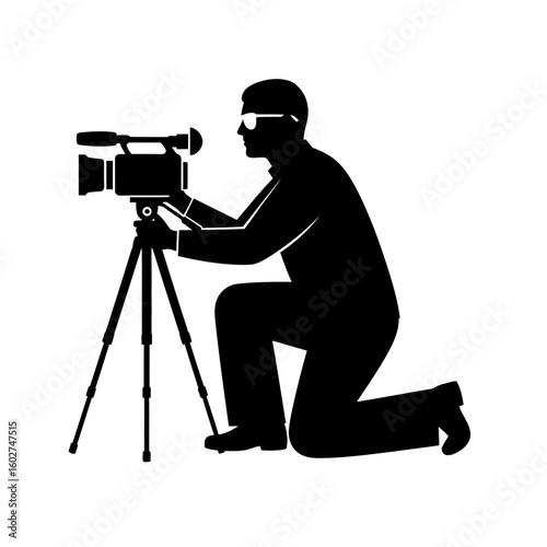 Silhouette of a kneeling cameraman with sunglasses operating a professional video camera on a tripod