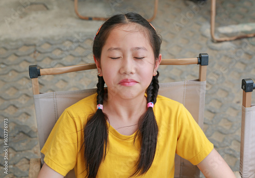 Close-up portrait of Asian young girl child age about 11 years old while sitting on chair and closed eyes.