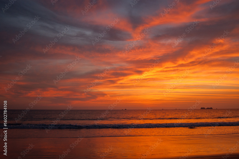 A vibrant sunset paints the sky with fiery hues of orange and red, reflecting on the tranquil ocean waters and sandy beach below, creating a breathtaking scene of natural beauty. A vibrant sunset paints the sky with fiery hues of orange and red, reflecting on the tranquil ocean waters and sandy beach below, creating a breathtaking scene of natural beauty.