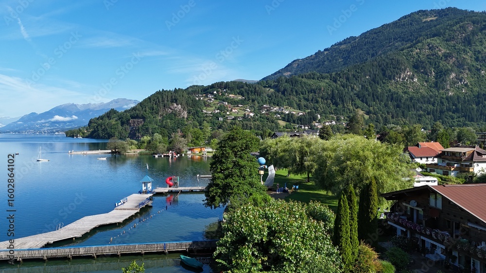 Naklejka premium Lakeside Promenade and Village with Wooden Piers and Mountain Backdrop in Summer