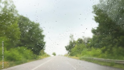 view from inside car window on rain water drops falling on glass with blurred trees nature background at summer spring day.