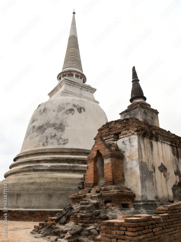 Fototapeta premium Ancient Thai stupas stand majestically against a cloudy sky, showcasing historical architecture white background