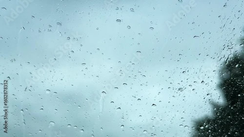 view from inside car window on rain water drops falling on glass with blurred trees nature background at summer spring day.