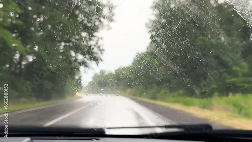 view from inside car window on rain water drops falling on glass with blurred trees nature background at summer spring day.