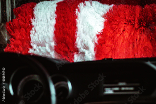 View from inside a car as red and white rotating brushes clean the windshield in an automatic car wash station.